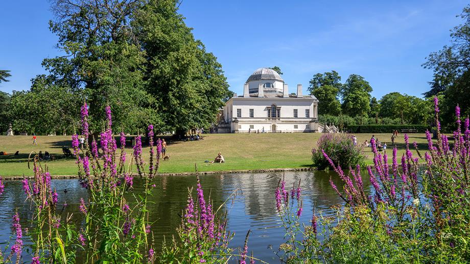 A peaceful river on a sunny day, with a beautiful villa in the background and purple flowers in the foreground