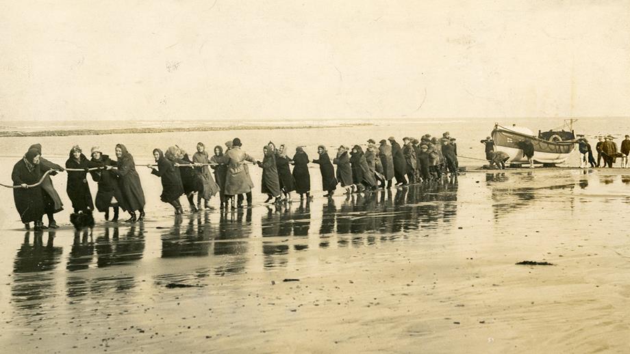 A sepia photograph showing more than 30 volunteers pulling a Huxley lifeboat