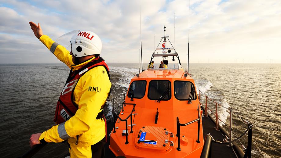 A crew member signals from the bow of a lifeboat during a man overboard training exercise