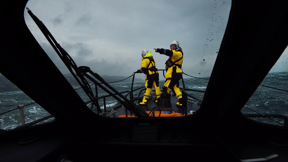 Two RNLI lifeboat crew members stand on deck during rough conditions