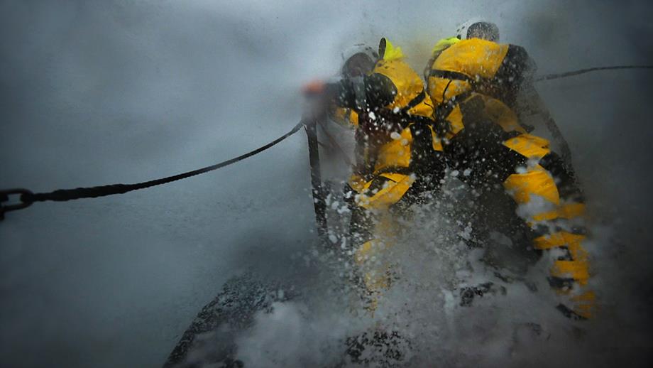 Two crew members on deck in heavy sea spray and rain