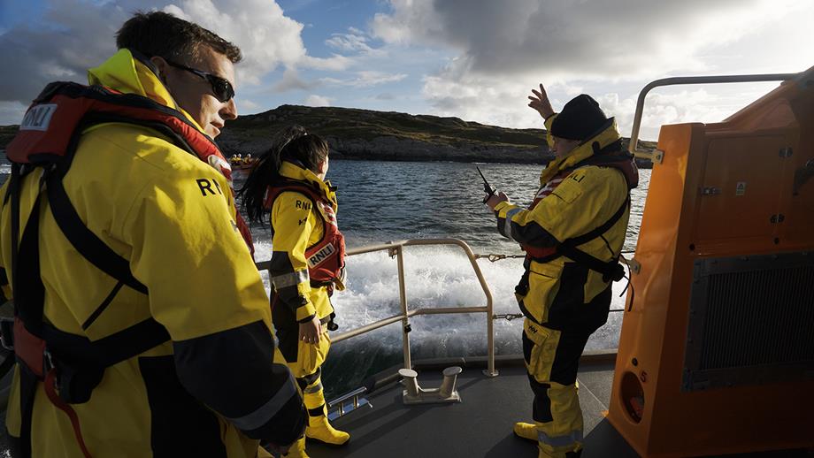 Three crew members from Clifden RNLI aboard their Shannon class lifeboat. One of the crew members is using a VHF radio. 