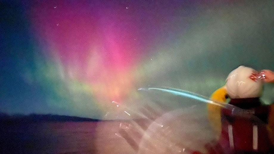 Two Kyle RNLI crew members look towards the blue, pink and green sky of the northern lights