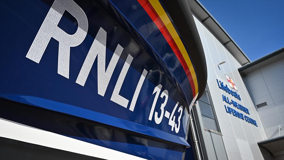 Close-up of the hull of a lifeboat in foreground, with the RNLI’s All-weather lifeboat Centre in background