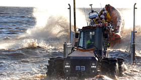A tractor, in shallow water, launches a B class inshore lifeboat out to sea