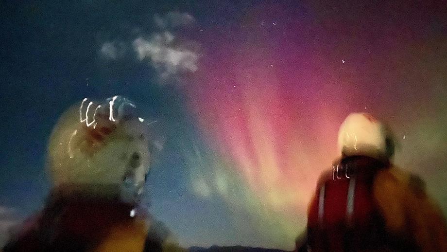 A large section of the sky glows pink with the aurora borealis