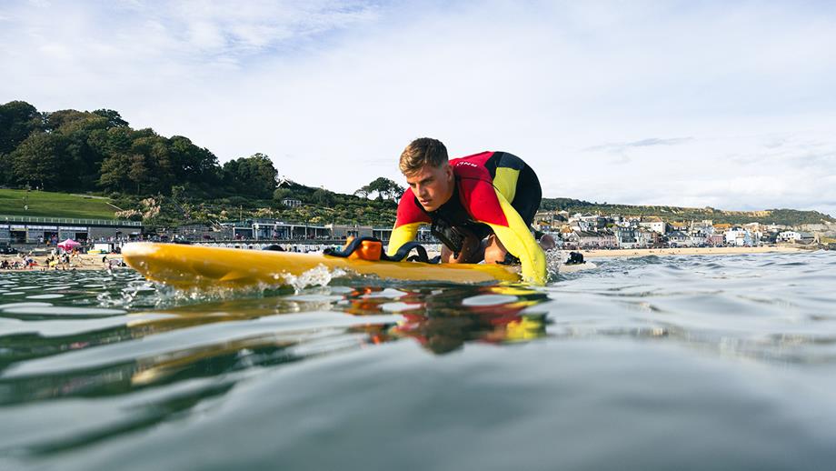 An RNLI lifeguard on a yellow rescue board, paddling out to sea