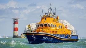 Yarmouth’s Severn class lifeboat passes by The Needles. There is one crew member at the front of the boat on the lower deck, and five crew looking out from the upper deck.
