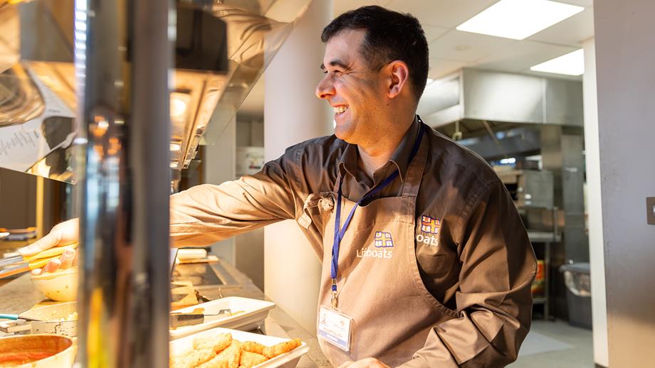 A staff member at the RNLI College serving breakfast, smiling 