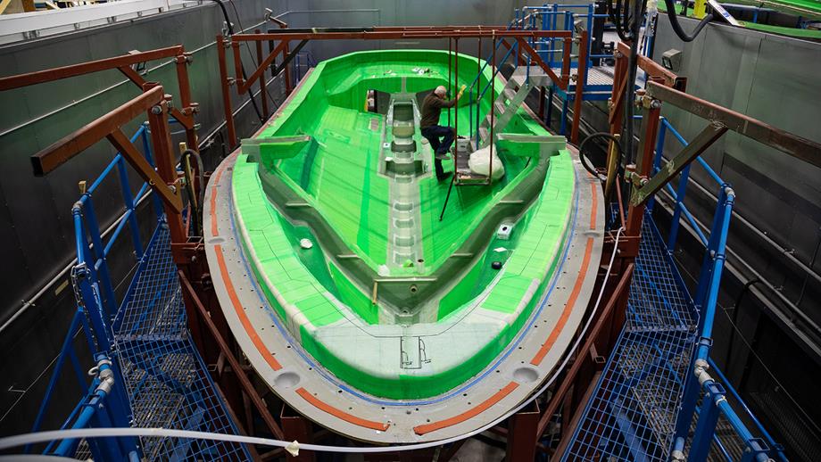 A Shannon class lifeboat’s hull is being constructed in the All-weather Lifeboat Centre. The hull is made of bright green composite material. 