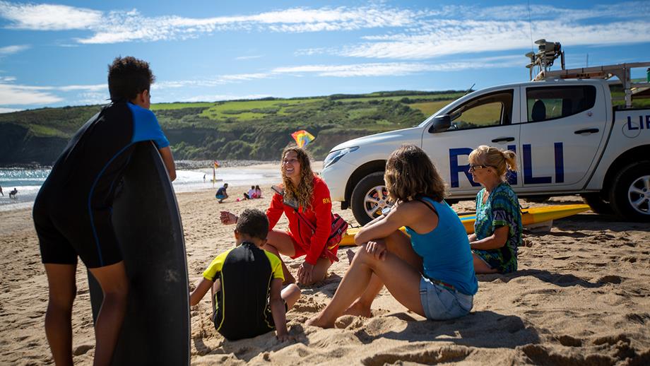 RNLI lifeguard giving safety advice to young family on Praa Sands beach, Cornwall