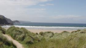 Farr Bay, with its long stretch of sand, grassy dunes, and a rocky cliff jutting out into the sea 