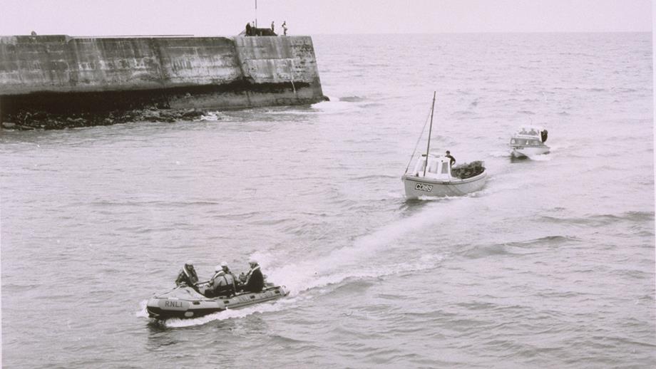 A black and white photograph showing Aberystwyth’s C class lifeboat towing two fishing boats. You can see the harbour wall in the background.
