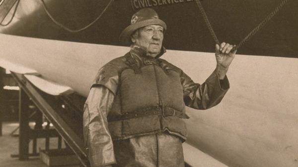 Coxswain Albert Emptage wearing oilskins and a sou’wester, standing alongside The Lord Southborough lifeboat