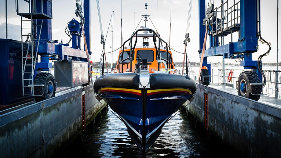 A navy blue and orange lifeboat is winched into the water at the All-weather Lifeboat Centre