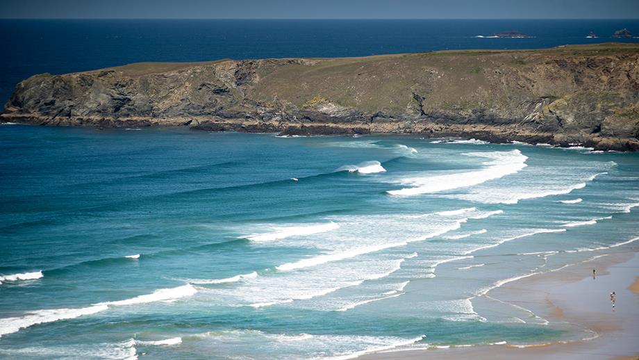 A Cornish bay edged by a rocky headland, with a rip current visible in the centre of the beach by the shoreline – an area of darker and deeper water where the waves are not breaking.