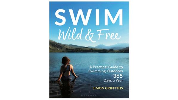 The cover of Swim Wild and Free by Simon Griffiths. It shows the back of a person with thick shoulder length brown hair wading into calm water in a green mountainous landscape on a bright blue day.