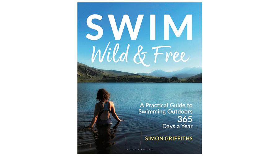 The cover of Swim Wild and Free by Simon Griffiths. It shows the back of a person with thick shoulder length brown hair wading into calm water in a green mountainous landscape on a bright blue day.