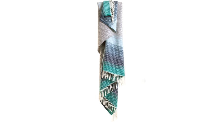 A woollen Woven Ombre Seaside Throw with blended lines in shades of blue along the tasselled edges and a soft grey in the centre