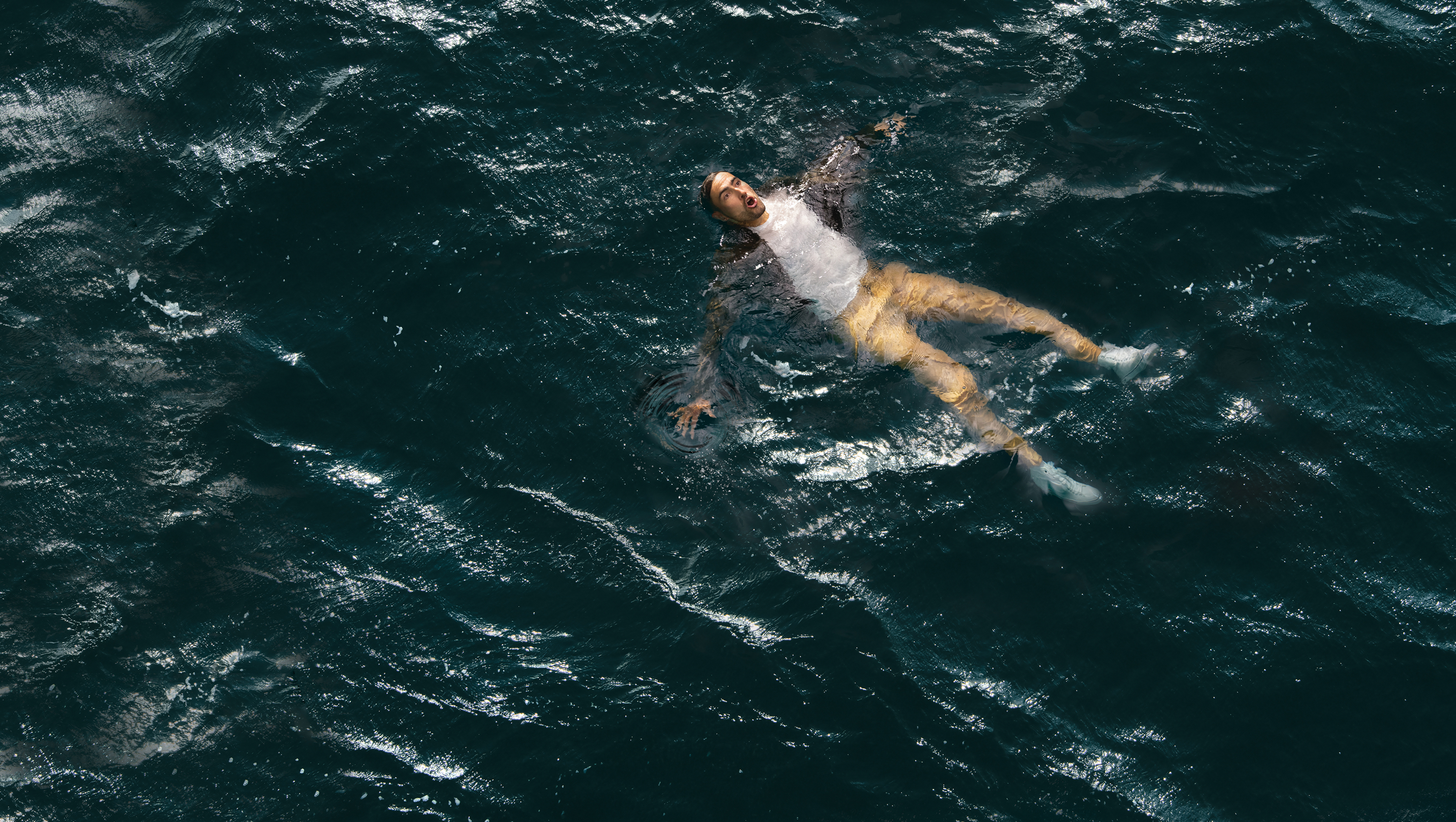 A man is floating in the sea, with his head tilted back and his arms and legs extended