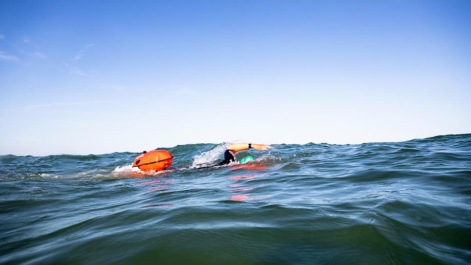 A swimmer in a wetsuit, with a bright orange tow float, in the sea