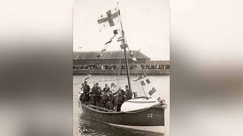 A black and white photograph of Queen Elizabeth the Queen Mother onboard Arbroath’s motor lifeboat, alongside her crew. 