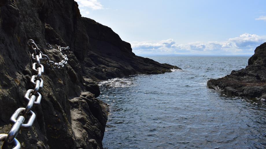 A close-up of one of the chains anchored into the cliff face on the Elie Chainwalk in Fife with the sea lapping the rocks below. 