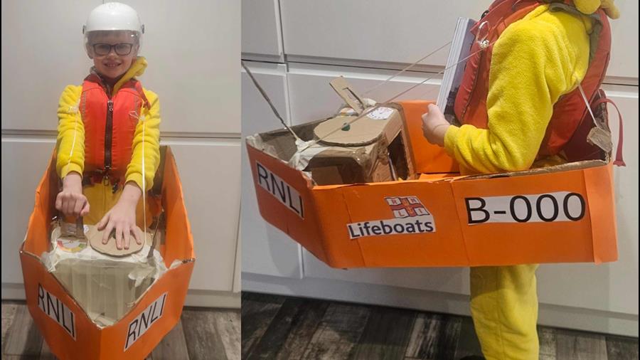Young RNLI lifeboat fan inside his homemade lifeboat crew member kit and orange cardboard lifeboat that he made for World Book Day