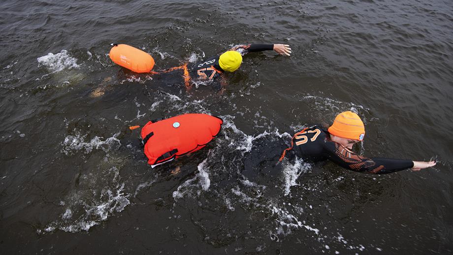 Two open water swimmers near Ballyglass. Wearing wetsuits, bright hats, and using tow floats