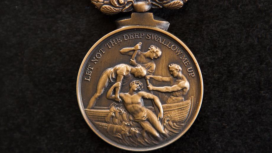The RNLI’s Bronze Medal for Gallantry, embossed with the phrase: ‘Let not the deep swallow me up’. The design portrays a man being pulled into a boat from the waves. 