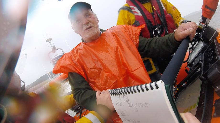 Allan sits on the Atlantic 85 inshore lifeboat, wearing an orange plastic top to keep the rain off him, waiting to be airlifted