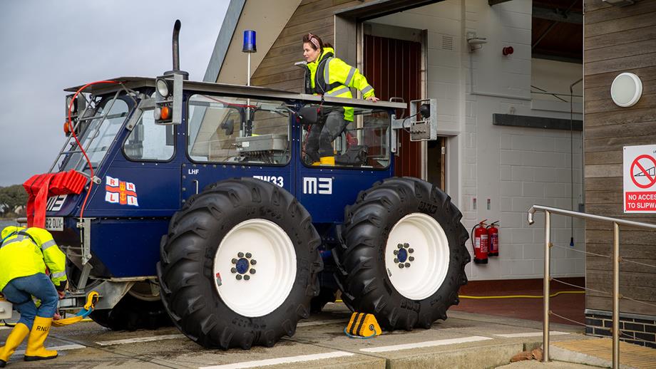 Lexi stands up at the back of the navy blue tractor, looking down the slipway. 