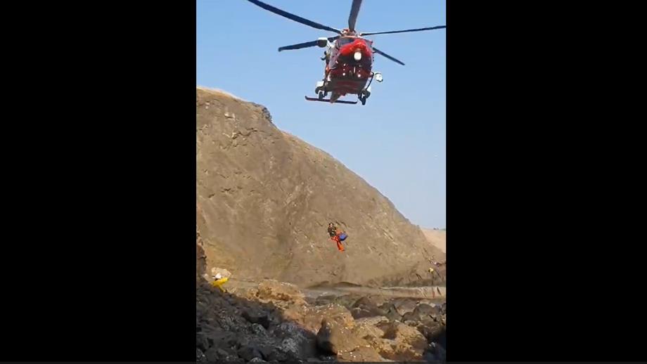 The Coastguard rescue helicopter hovers over the cliff as a paramedic and Jo are winched up into it. Anstruther Lifeboat Crew Member Stuart Hoggan is watching from the rocky shore.