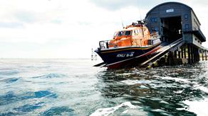 Bembridge’s all-weather Tamar class lifeboat launches from a slipway into calm seas on a bright cloudy day.