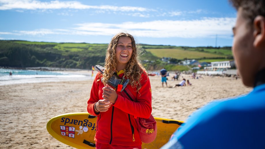 A female lifeguard is smiling and talking to a young boy on the beach.