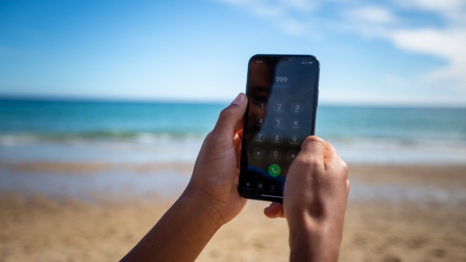 A phone with 999 being dialled, a beach in the background.
