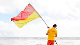 Lifeguard holding red and yellow flag at the beach showing casing lifeguards on duty