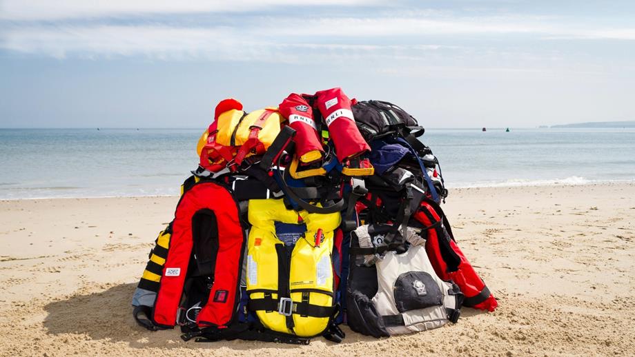 A pile of lifejackets on a sandy beach, with the sea in the background.
