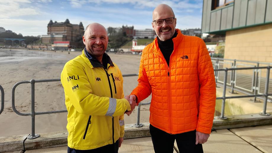 Michael Whiteley and Scarborough Coxswain Lee Martin are reunited after Michael was rescued by the RNLI. In the photograph, they’re shaking hands in front of the lifeboat station.