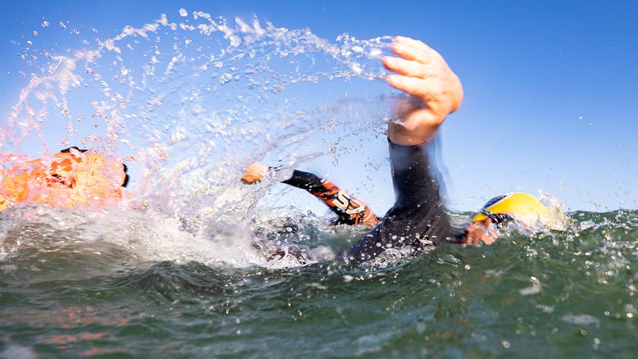 A swimmer’s arm splashes through the open water, with sea spray