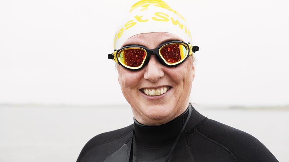 A swimmer wearing a yellow and white swimming cap and gold goggles grins at the camera