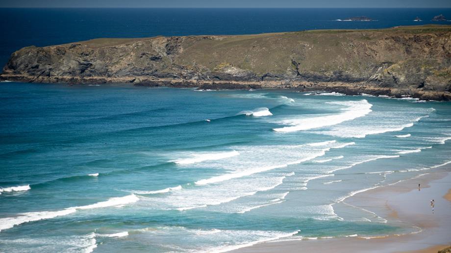 A beach with waves and steep cliffs on a sunny day