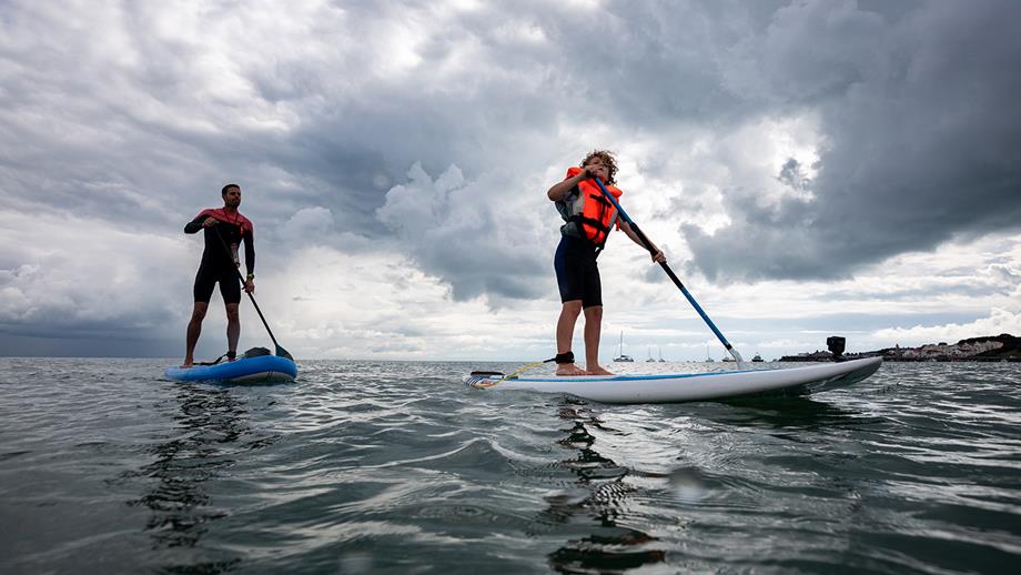 Two paddleboarders, wearing wetsuits and buoyancy aids, paddling on the sea