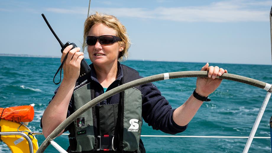 Yacht sailing: Crew member at the helm of a yacht talking into a handheld radio