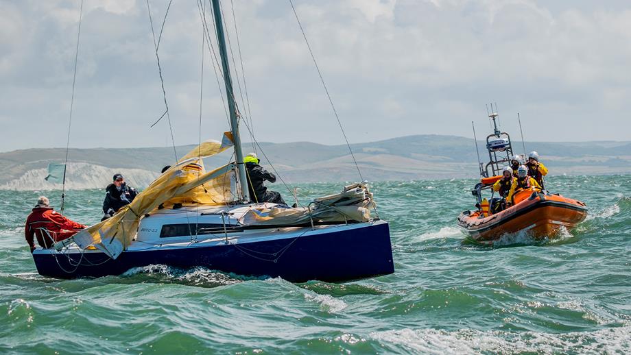 A sailing boat is at sea on a sunny day with an RNLI lifeboat next to it.