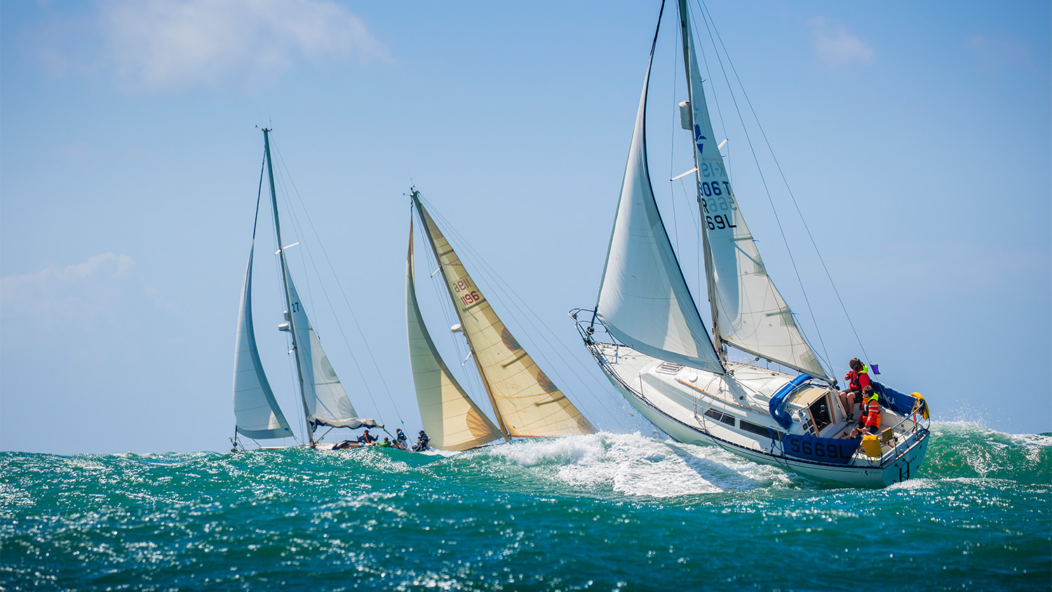 Three yachts are at sea on a beautiful sunny day.