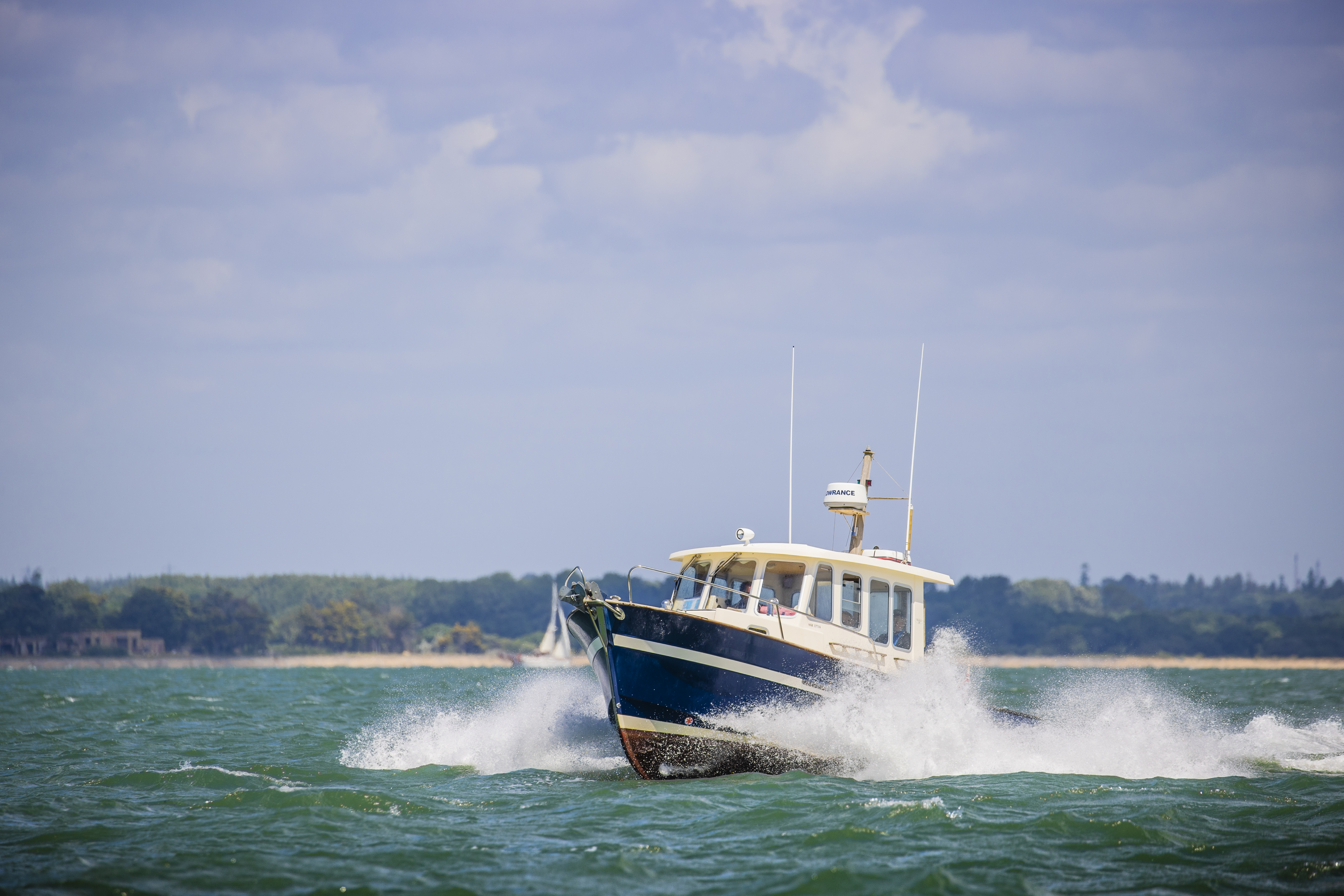 A navy and white motorboat out at sea on a sunny day, with lots of white spray.
