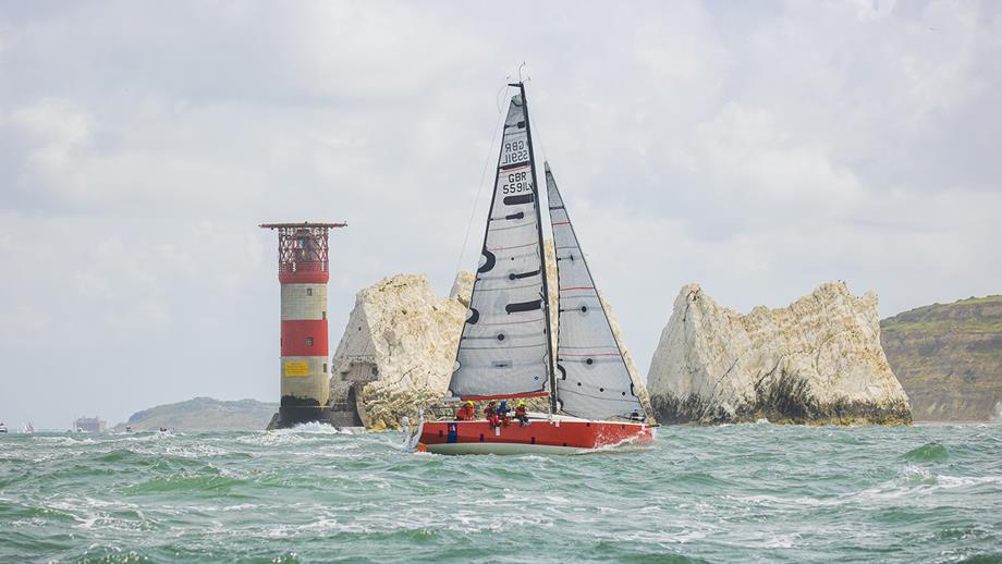 A sailing boat in front of a rocky outcrop and lighthouse