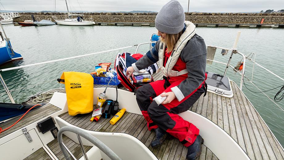A young female sailor sits aboard her boat and sorts through her kit, which includes sun cream, a VHF radio and snacks