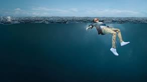 A young man is fully clothed in the open water. His face is above the water, looking up to the sky, and his arms and legs are stretched out, gently moving to help him stay afloat.